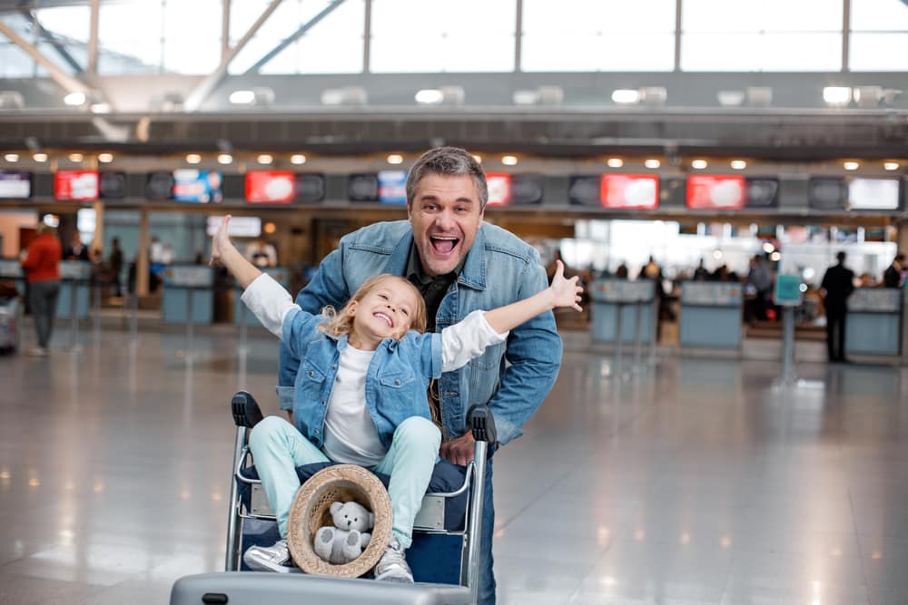 What You Need To Know About Fit To Fly Certificates: Mature man pushing daughter on trolley through airport