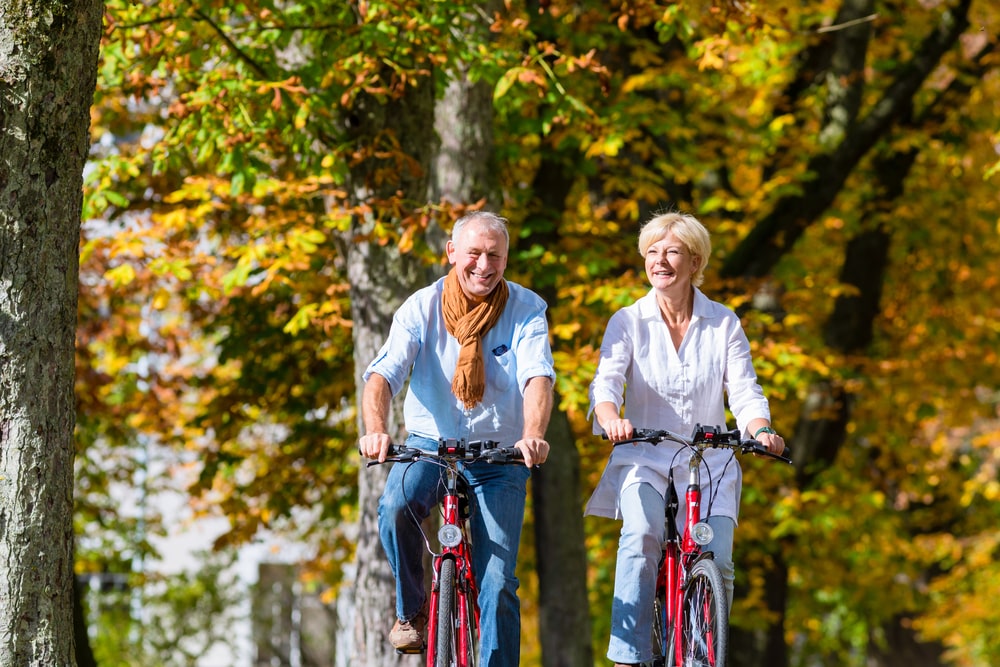 Do you need cycling holiday insurance? Middle aged couple cycling through forest in sun