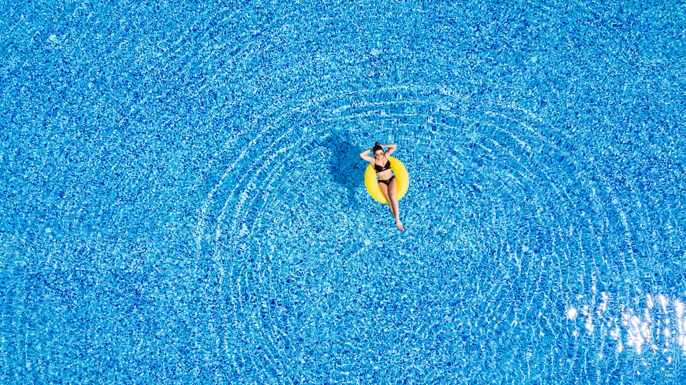 Travel Vaccinations Guide: Young woman relaxing on inflatable donut in swimming pool on holiday