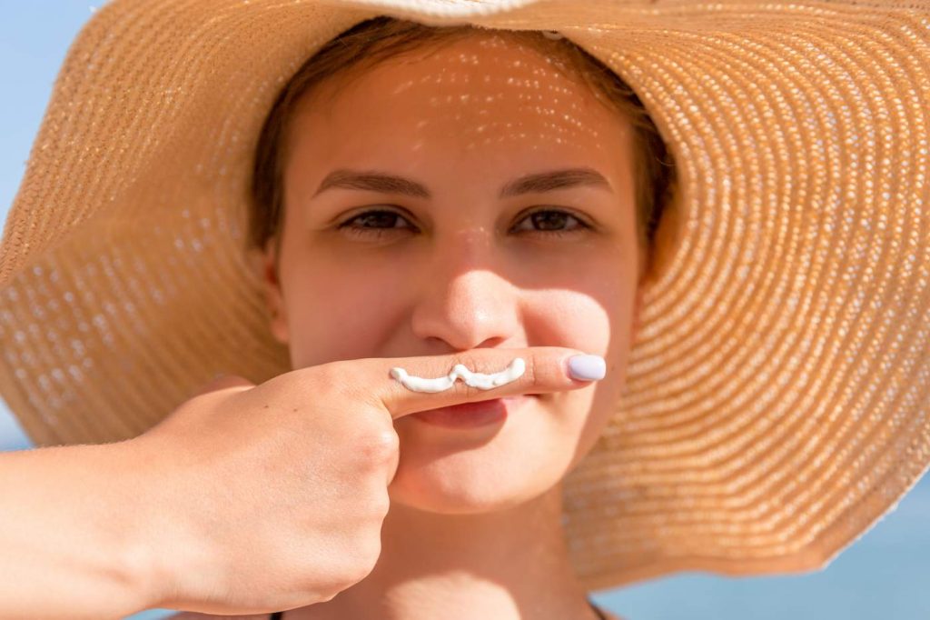 A young woman with a sun cream Movember moustache on her finger