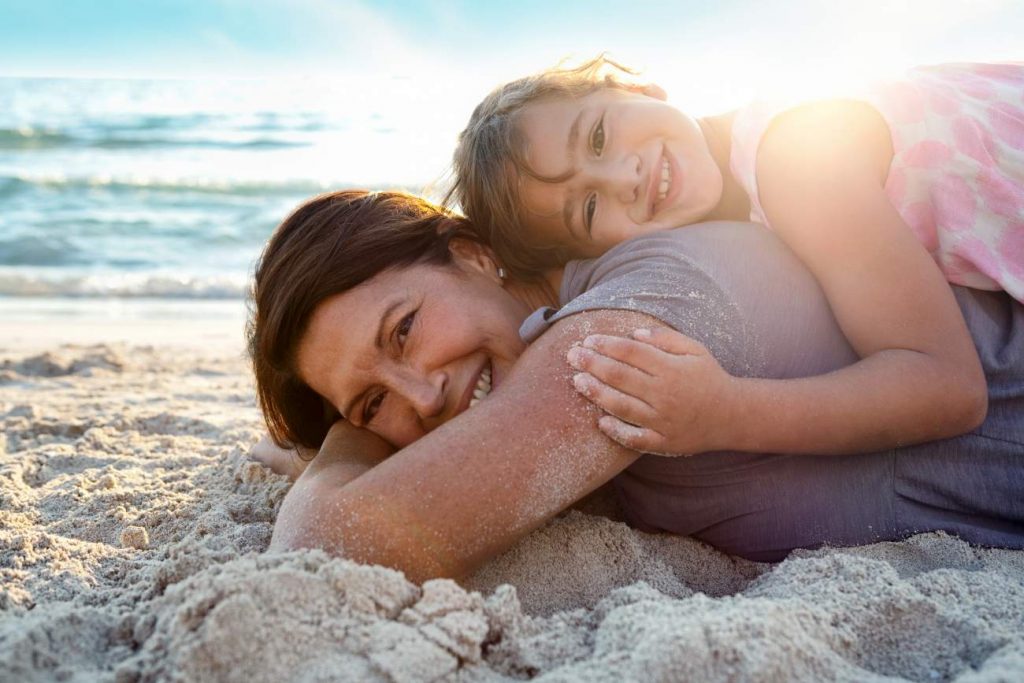 Tips for Travelling with Grandchildren: Grandmother laying on beach with grandaughter on holiday