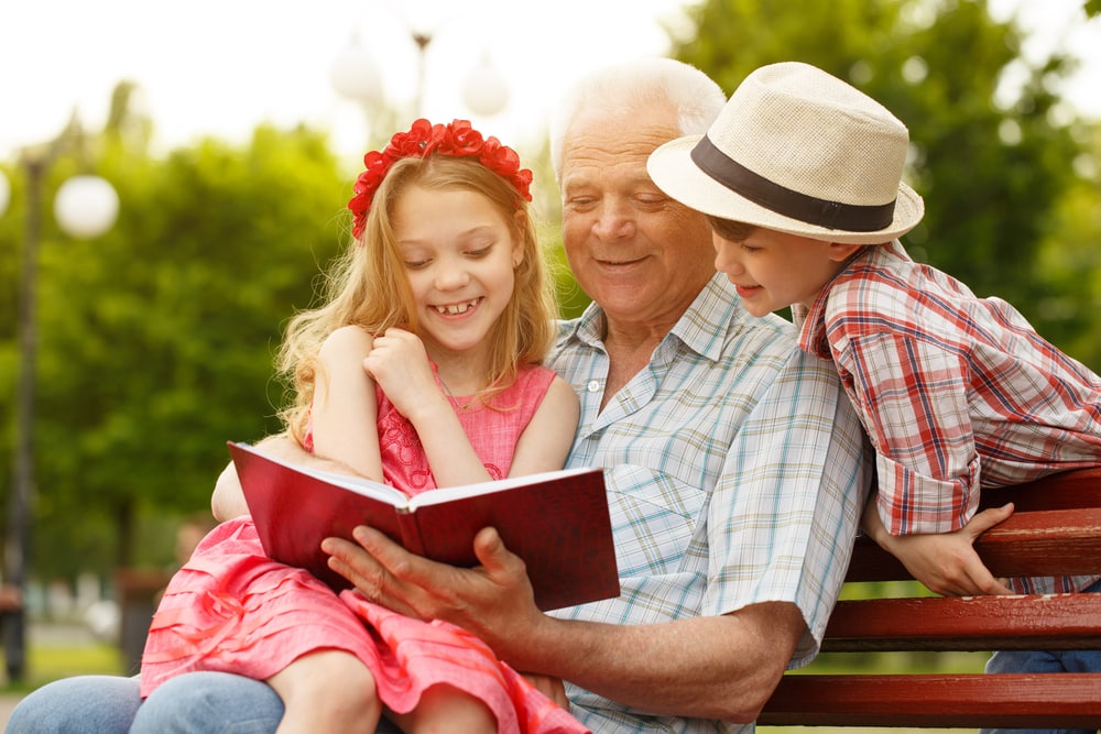 15 books to read on your holiday in 2019: Grandfather reading book to children on bench