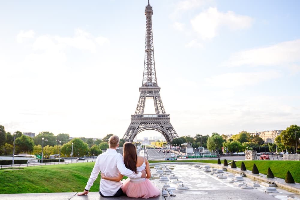 Do I Need Travel Insurance? Is It Worth It? Couple sitting at Eiffel tower, in Paris